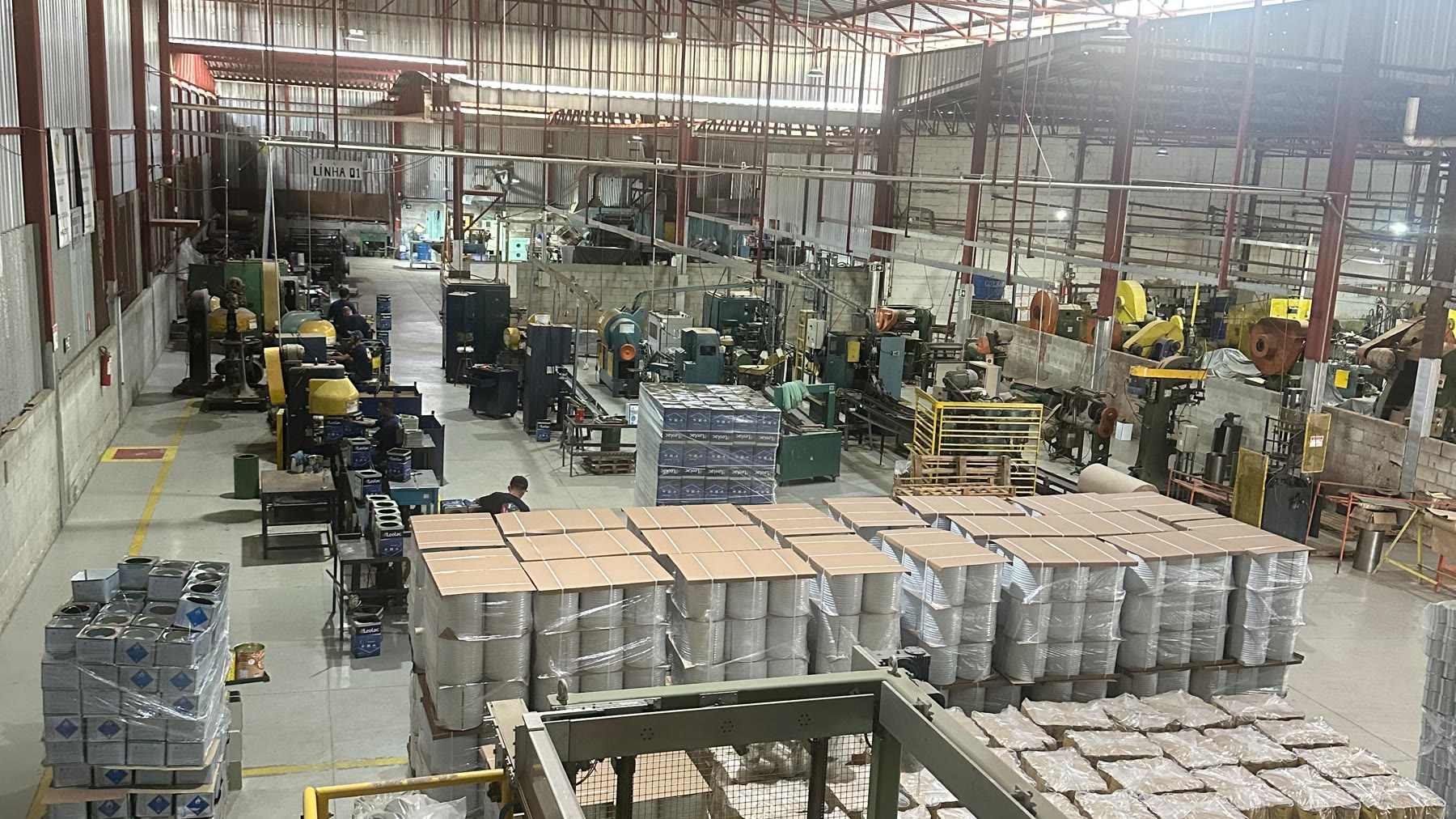 Vista interna da fábrica da EMB Embalagens em Minas Gerais, com linhas de produção e paletes de latas prontas