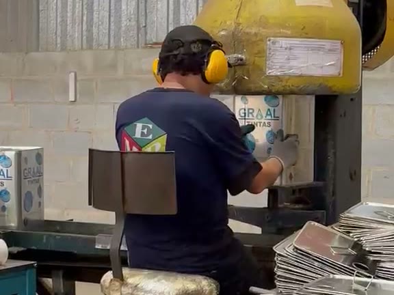 Operador da EMB com EPI conduzindo prensa na linha de produção de latas